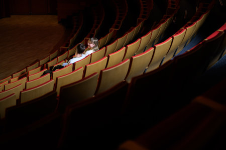 Young teenager couple in love at cinema having fun watching a film in the empty movie place. Entertainment and people concept.の写真素材