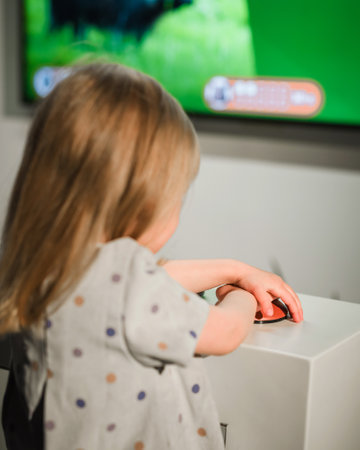 Toddler girl looking at a big television screen with interactive content, playing a knowledge game.の写真素材
