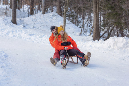 Joyful couple slides on a snow sled through a beautiful snowy forest