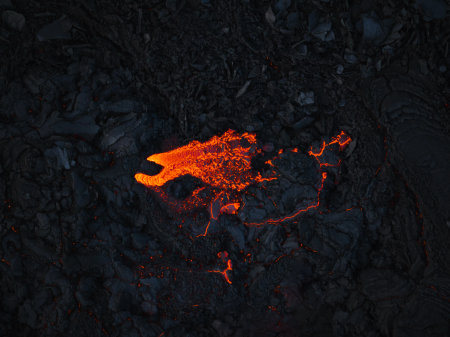 Streams of red hot lava flowing during a volcano eruption, toxic smoke covering the volcanic black field, aerial shot. Concepts of abstract patterns and backgrounds.の写真素材