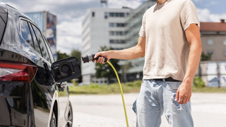 Man opening a socket and putting a charger in a black electric car at an EV charging station placed on city streetの写真素材
