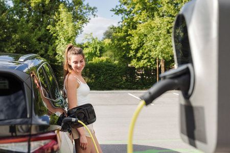 Young woman charging electric car parked in the city with renewable energy.の写真素材