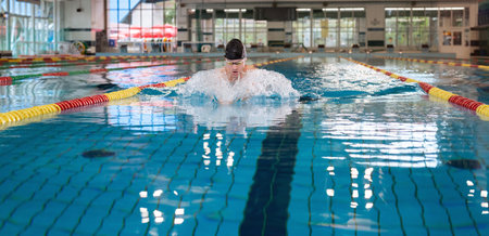 Front view of a male athlete swimming breaststroke style in the pool between two swimming lane...