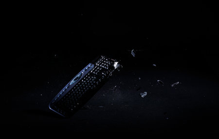 Cracking and crashing computer keyboard by smashing on the floor, isolated on a black background,...