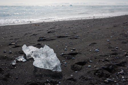 Ocean waves lapping up chunks of ice sparkling in the sun on a black sand beach. Natural wonder,...