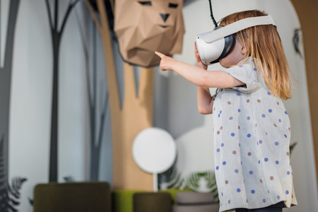 Adorable toddler girl with a virtual reality headset standing in a natural history museum playroom. Concept of children and modern technologies.の写真素材