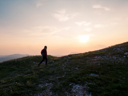 Female hiker silhouette with a backpack walking and following the trail uphill, enjoying the sky at sunset. Inspiration and healthy lifestyles concepts.の写真素材
