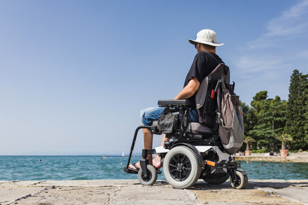 Tourist man with a disability sitting on the dock and looking at the open sea. Wheelchair travel and accessible tourism concept.の写真素材