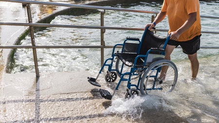 Male assistant helping a man in a wheelchair to enjoy the sea on an access ramp into the water. Accessible beach concept.の写真素材