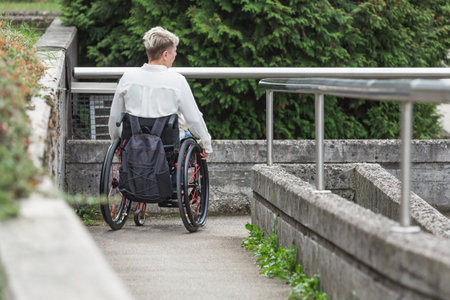 Person with physical impairment operating a wheelchair along an accessible ramp to access the...