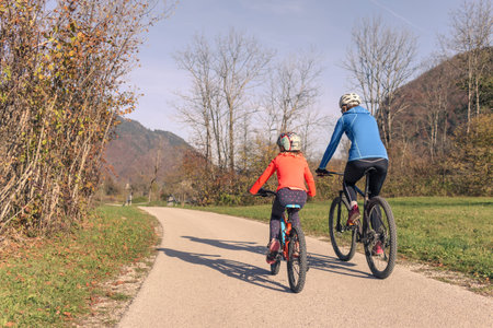 Two cyclists, a mother with a girl child on a bike ride along the road in rural nature. Family recreation concept.の写真素材