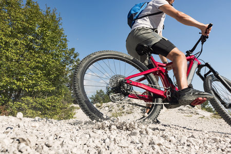 Mountain bike rider riding an electric bike along a white gravel trail on a sunny summer day....