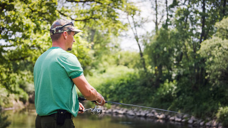 Young fisherman fishing on the river bank surrounded by beautiful green nature, using small fish as...