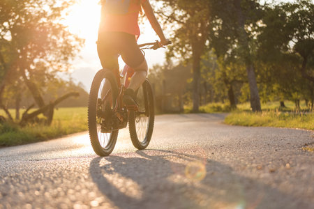 Female silhouette riding an electric mountain bike along the countryside road at a beautiful sunset