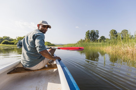 Smiling young man enjoying holiday travel activity on the lake, paddling a canoe and relaxing surrounded by peaceful summer nature.の写真素材