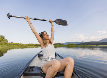 Active young woman paddling a canoe on a lake surrounded by green summer nature, close up shot. Canoeing, therapy, and recreation concepts.の写真素材