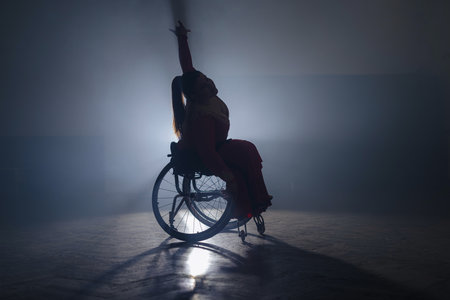 Woman dancing in a wheelchair, on a black background with backlight. Disability, sport, and life inspiration concepts.の写真素材