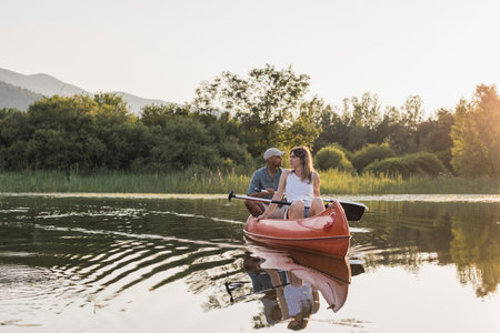 Couple canoeing on calm lake water at sunset enjoying the tranquility of surrounding green nature and colorful sky view.の写真素材