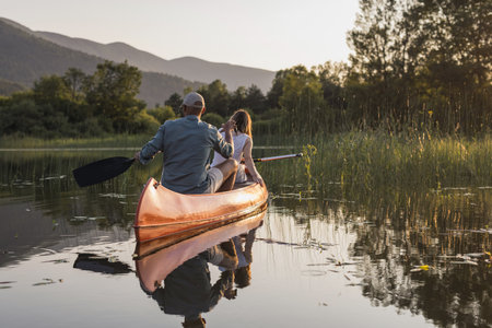 Smiling couple relaxing while canoeing on a calm lake at sunset, enjoying beautiful green natural surroundings.の写真素材