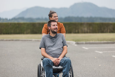 Personal assistant helping a man with disability to push a wheelchair outdoors. Help service...