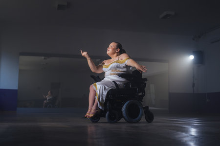 Female dancer, an electric wheelchair user performing graceful dance moves during training in a...