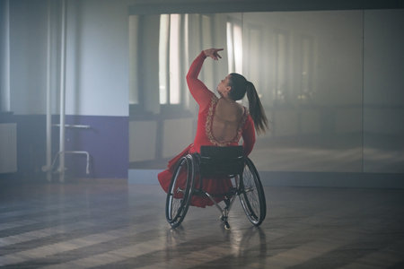 Woman with a disability, a para dancer practicing choreography at the dance studio, making wheelchair spin and elegant arm moves.の写真素材
