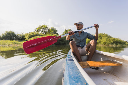 Young man canoeing, paddling, and moving canoe through the lake water, enjoying the natural...
