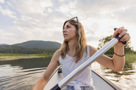 Young woman relaxing while paddling a canoe on a calm lake, enjoying the green natural environment. Canoeing concept.の写真素材