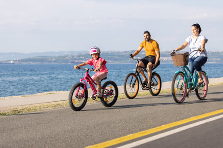 Mother, father and girl child having fun on vacation cycling near the sea. Family coastal bike ride.の写真素材