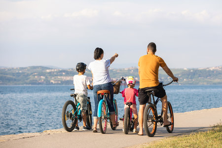 Two children with their parents, recreational cyclists, taking a break and looking at the seascape on a clear summer dayの写真素材