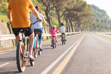 Family of four, parents with son and little daughter relaxed cycling on a coastal route, with a view...