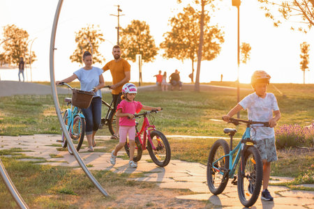 Young family with two children with bicycles walking through a park at sunsetの写真素材