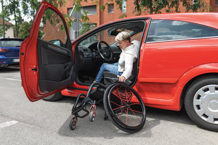 Female driver with physical impairment getting out from car and transferring into the wheelchair. Disability and mobility concept.の写真素材