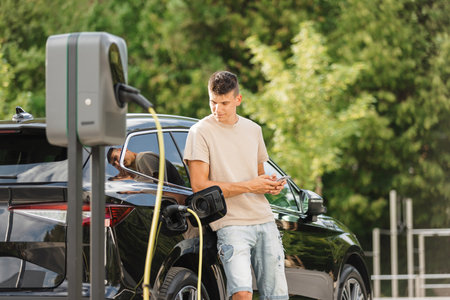 Men charging electric car in city and adjusting EV charging app on smartphoneの写真素材