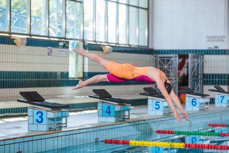Professional sportswoman taking a solid stance on the starting block, dive off and hit the pool water.の写真素材