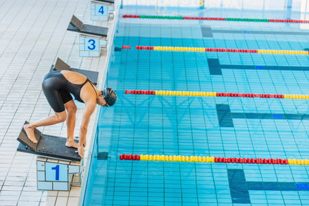 Professional female swimmer preparing and jumping off the starting block into the pool. Competitive swimmers workout concept.の写真素材