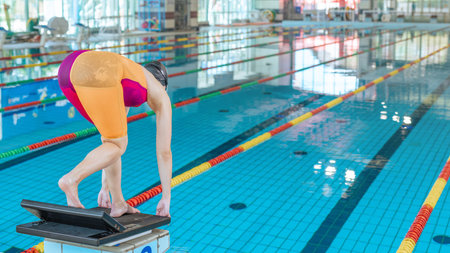 Professional sportswoman taking a solid stance on the starting block, dive off and hit the pool water.の写真素材
