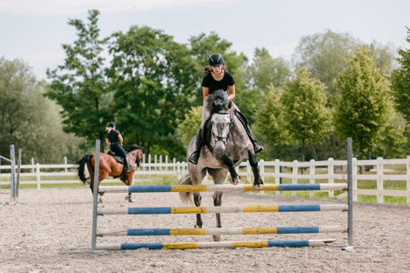 Girl on a dapple gray horse practicing jumping over a log fence in the drill hall of the equestrian center. Showjumping and eventing concepts.の写真素材