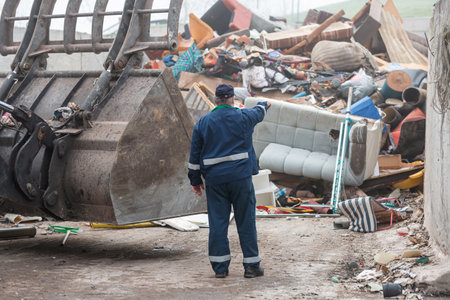 Male worker pointing on wheel loader and the garbage heap at a landfill site, rear view. Waste disposal, consolidation, and transfer concept.の写真素材