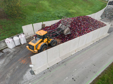 Yellow skid steer loader grabbing candle waste with scrap grapple on a big heap at the recycling...