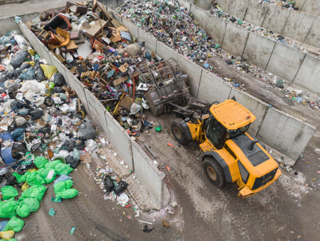 Handling construction waste on the landfill site, skid steer loader scooping and dumping dusty trash, aerial side view.の写真素材