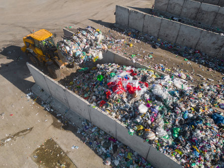 Yellow skid steer loader moving waste material, shaking out a grapple on the garbage heap in the...