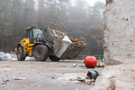 Yellow wheel loader, with lifted scrap grapple, moving along the recycling center area in process...