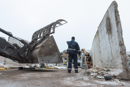 Male worker pointing on wheel loader and the garbage heap at a landfill site, rear view. Waste...