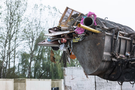 Yellow skid steer loader moving wooden waste material, shaking out a scrap grapple on the garbage heap in the materials recovery facilityの写真素材