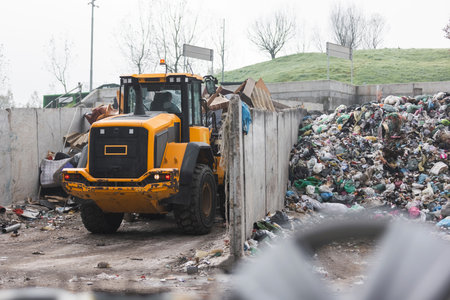Yellow skid steer loader moving wooden waste material, shaking out a scrap grapple on the garbage...