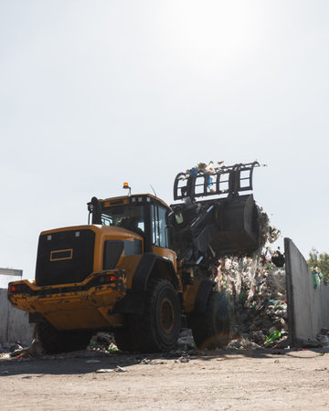 Yellow wheel loader, with lifted scrap grapple, moving along the recycling center area in process handling dumped wasteの写真素材