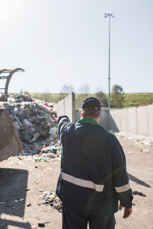 Landfill worker directing skid steer loader on the garbage heap. Waste disposal, consolidation, and...