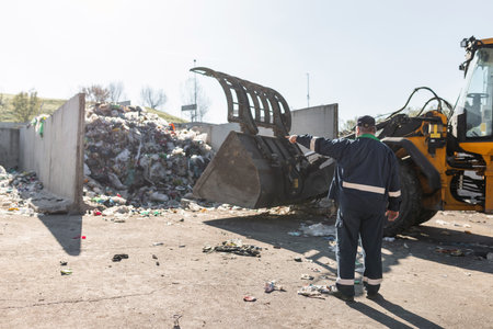 Landfill worker directing skid steer loader on the garbage heap. Waste disposal, consolidation, and transfer concept.の写真素材