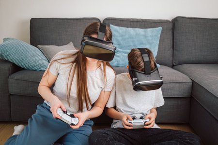 Mother and son enjoy entertainment video gaming together, using VR goggles and controllers while...